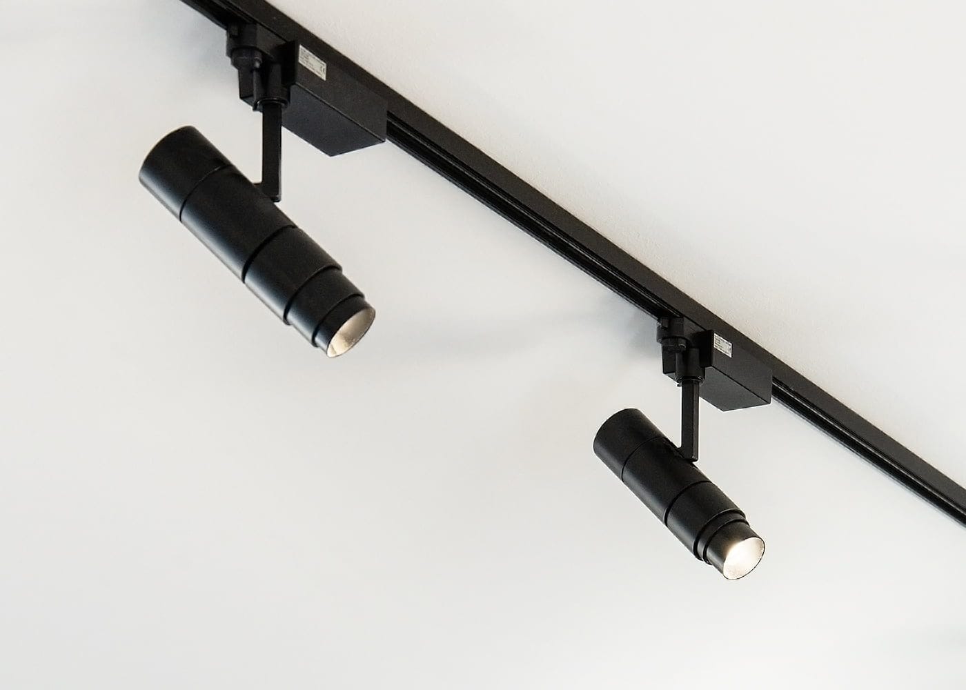 Minimalistinen kokoonpano kahdella mustalla sylinterimäisellä LED-kiskovalolla valkoisella katolla, kiinnitettynä mustaan kiskoon, esittelee modernia valaistussuunnittelua ja säädettäviä kulmia.