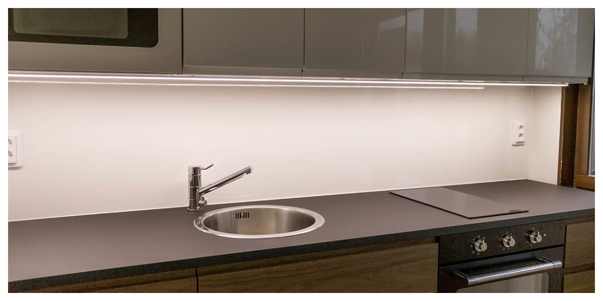 Moderni keittiö, jossa LED-kaappivalaistus, tyylikäs tumma työtaso, ruostumattomasta teräksestä valmistettu pesuallas, yksikahvainen hana, valaiseva liesitaso ja kiiltävät kaapit.