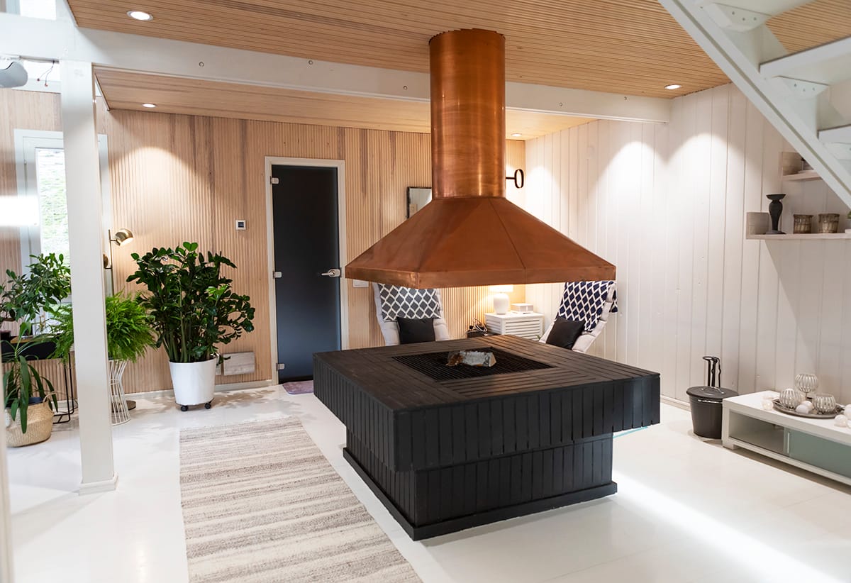 Moderni olohuone, jossa keskellä musta ja puutakka, kuparipiippu, LED-valaistus, pehmustetut tuolit, viherkasveja ja tyylikäs sisustus.