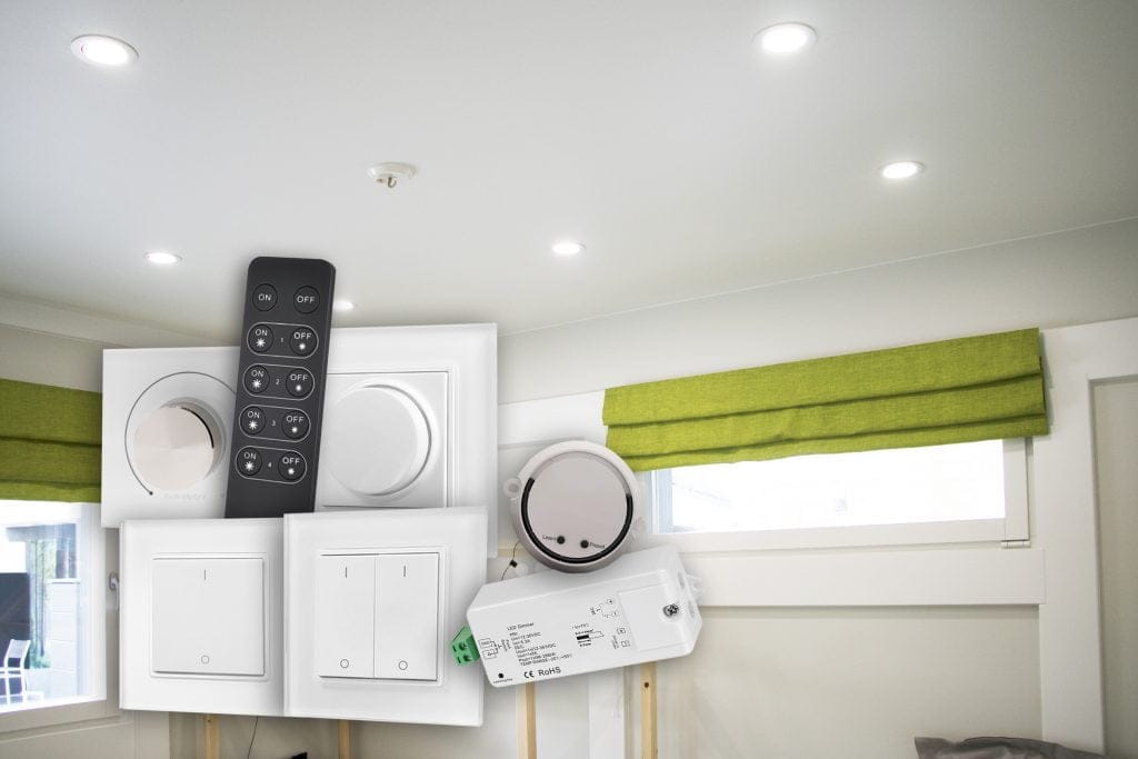 Huoneessa upotetut LED-kattovalot, vihreät kaihtimet ikkunassa ja erilaisia sähkökytkimiä ja kaukosäädin esillä.