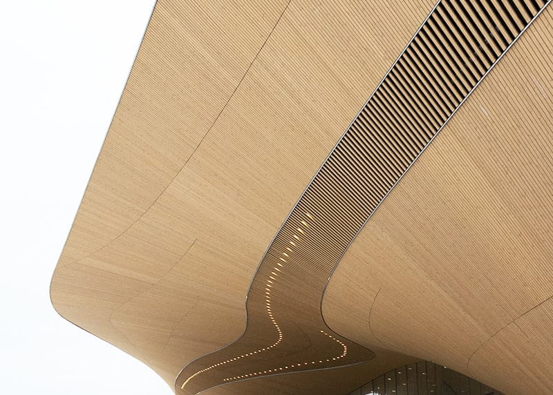 Kaareva puukuvioinen rakenne, jossa on aaltoileva muotoilu ja upotetut LED-valot, jotka korostavat modernia abstraktia ilmettä valkoista taustaa vasten.